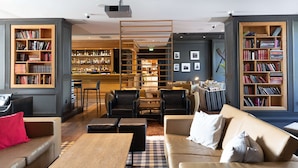 A modern lounge area with a bar, multiple seating options including sofas and chairs, and two large bookshelves filled with books. - Scandic Helsinki Aviacongress (Vantaa)