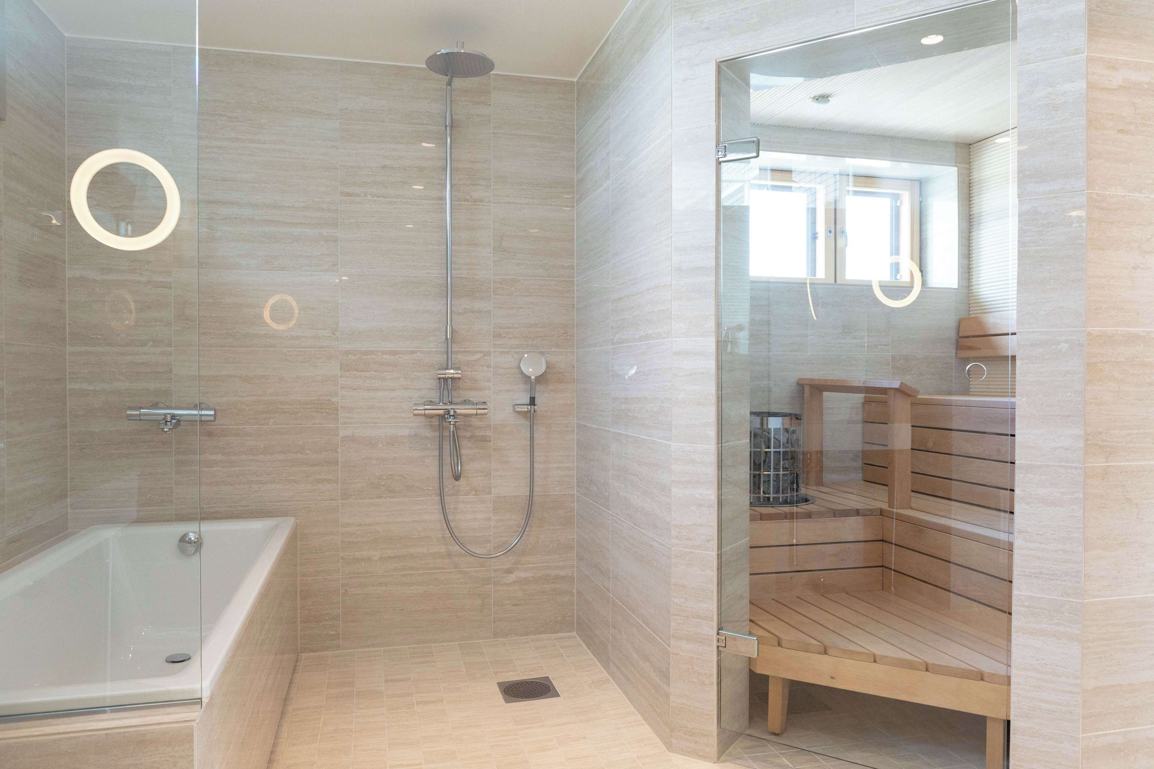 A modern bathroom with a glass-enclosed shower, a standalone bathtub, and a wooden sauna bench.