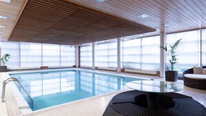 A modern indoor pool area with clear glass walls, a wooden ceiling, and a seating area with a round table and chairs. - Scandic Helsinki Aviacongress (Vantaa)