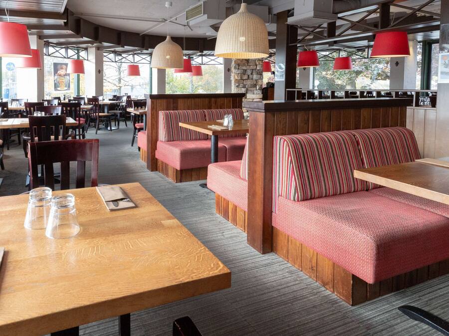 A restaurant with wooden tables and red upholstered booths, large pendant lights, and a stone wall.