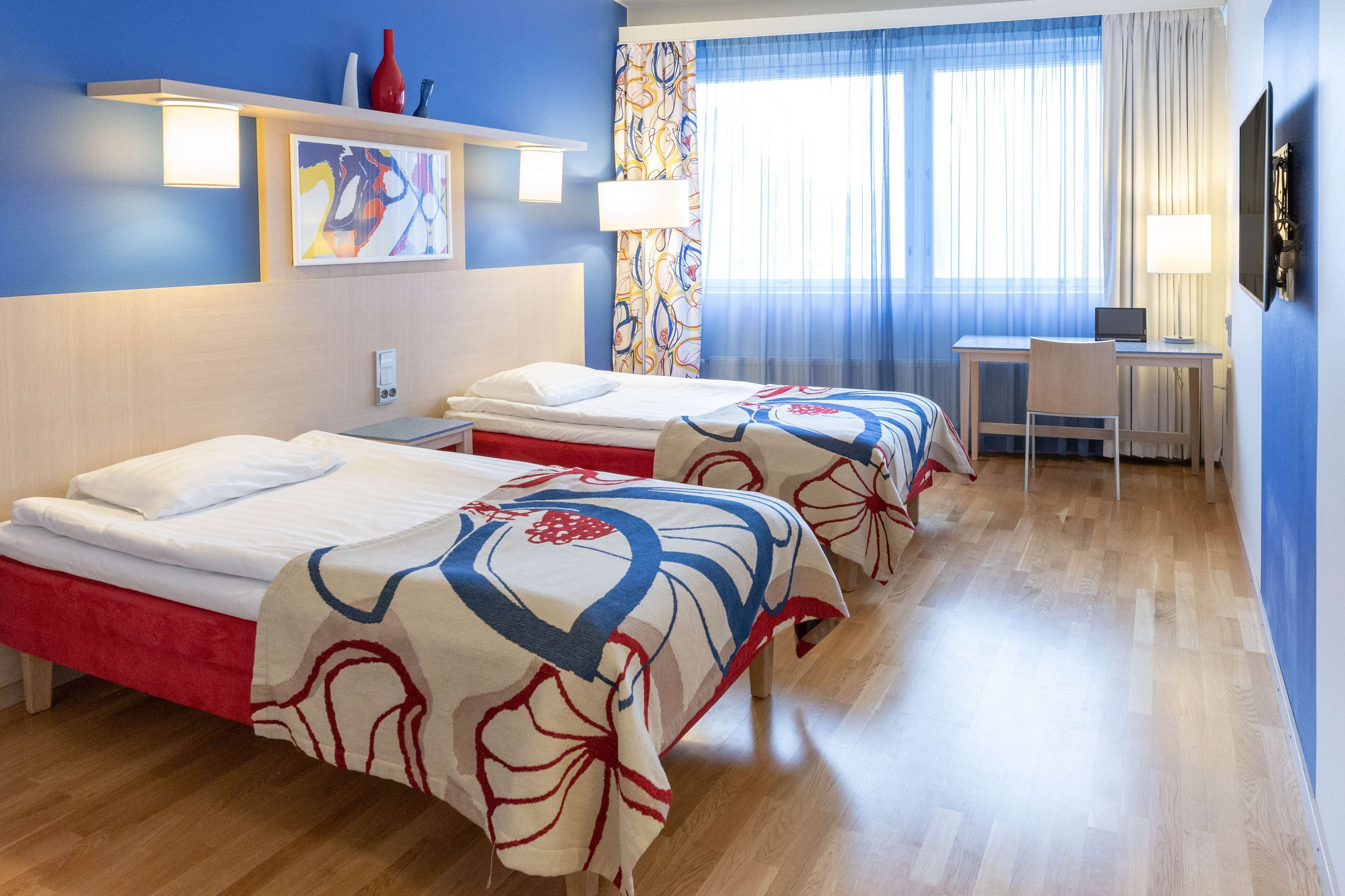 A hotel room with two beds, a desk, and a TV.