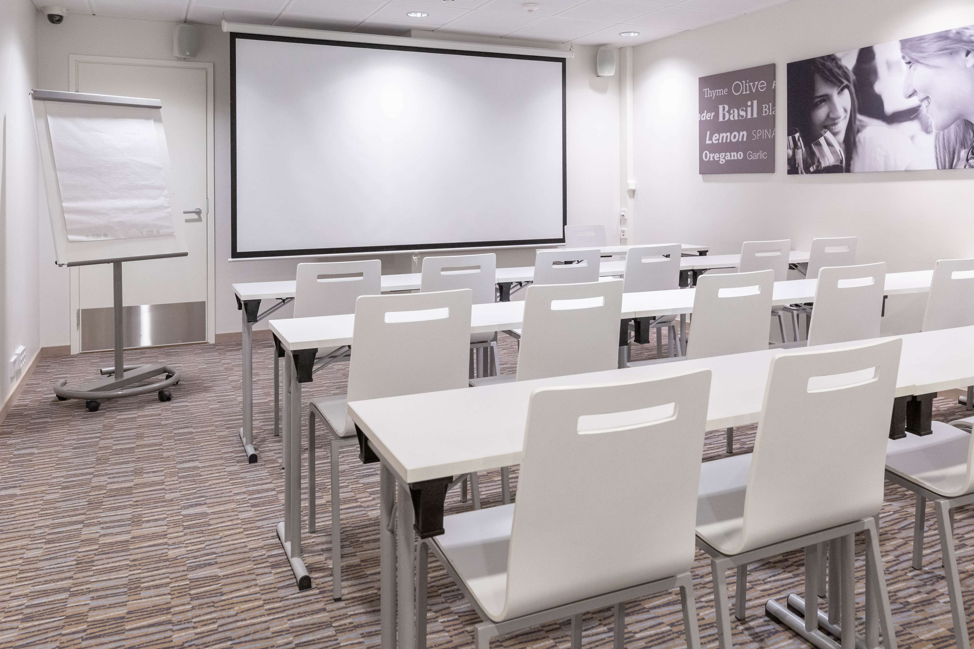 Un salón de conferencias con una pantalla grande, sillas blancas y mesas.