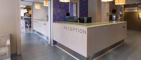 A reception area with a glass counter, a clock, and a directional sign to the breakfast room.