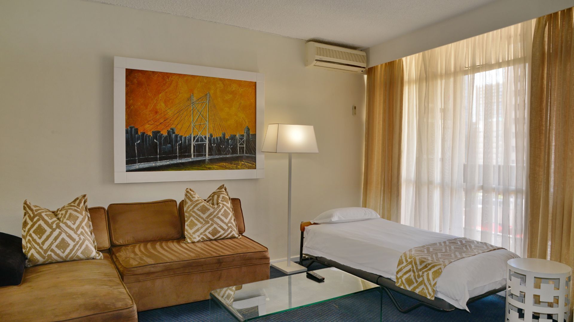 A hotel room with a bed, a sofa, a coffee table, a lamp, and a painting on the wall.