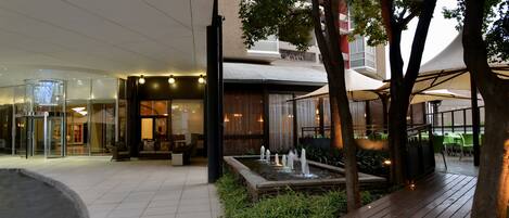 A modern building with a glass entrance, outdoor seating, and a water feature.