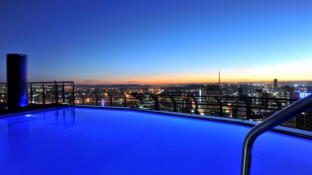 Una piscina en la azotea con vistas a un paisaje urbano al atardecer.