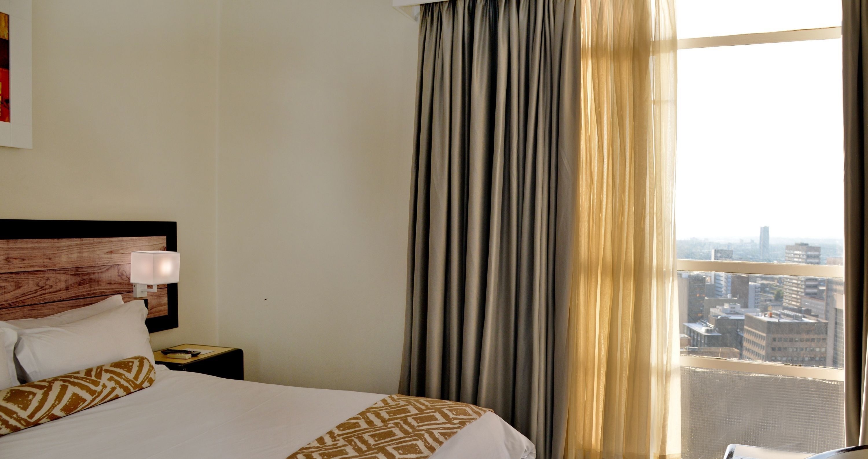 Una habitación de hotel con una cama, una mesita de noche, una lámpara y una ventana con cortinas.