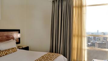 A hotel room with a bed, a nightstand, a lamp, and a window with curtains.