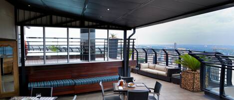 A rooftop terrace with a dining area, seating, and a view of the cityscape.