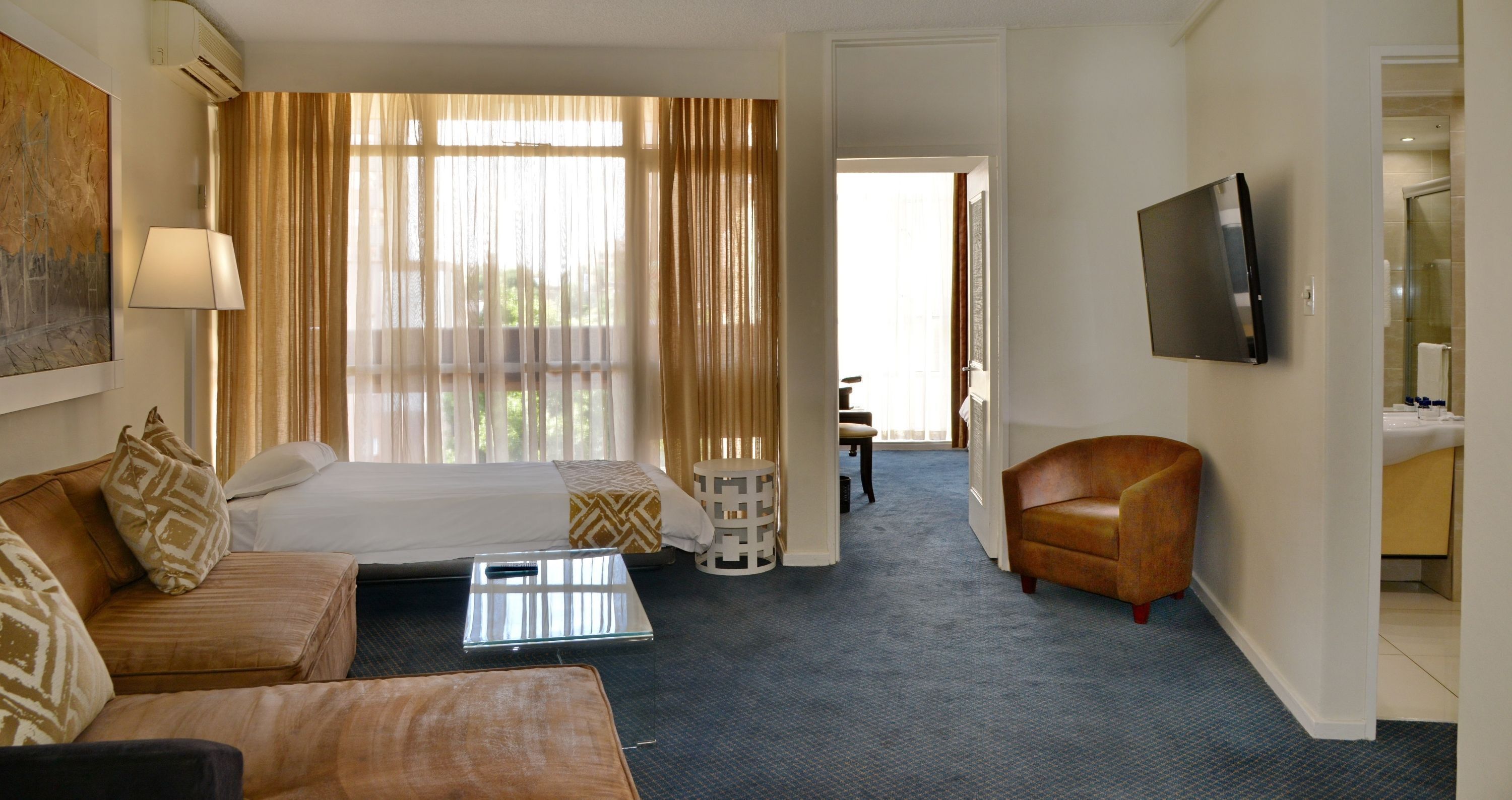 A hotel room with a bed, a sofa, a coffee table, a TV, and a bathroom visible through an open door.
