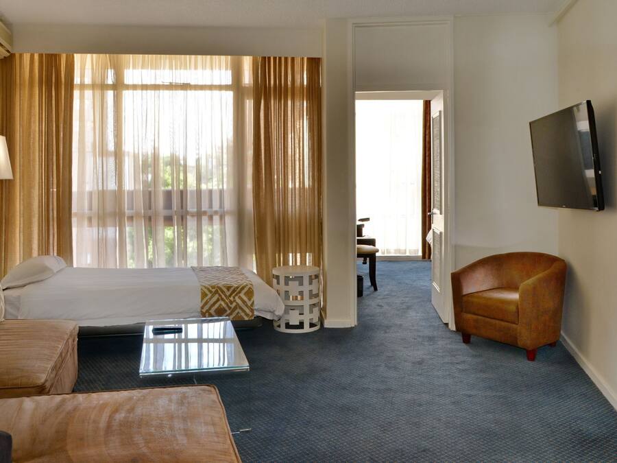 A hotel room with a bed, a sofa, a coffee table, a TV, and a bathroom visible through an open door.