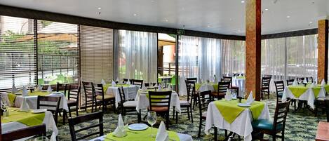 A restaurant with multiple tables set for dining, featuring green tablecloths and white napkins.