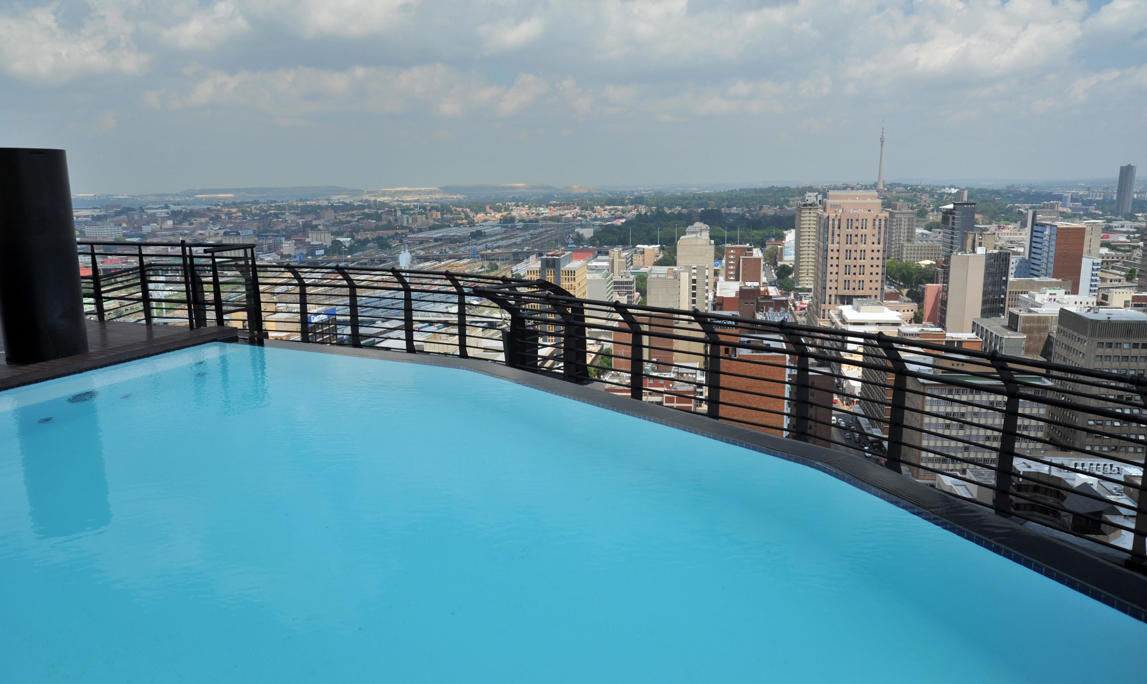 A rooftop pool with a city view, a metal railing, and a clear sky.