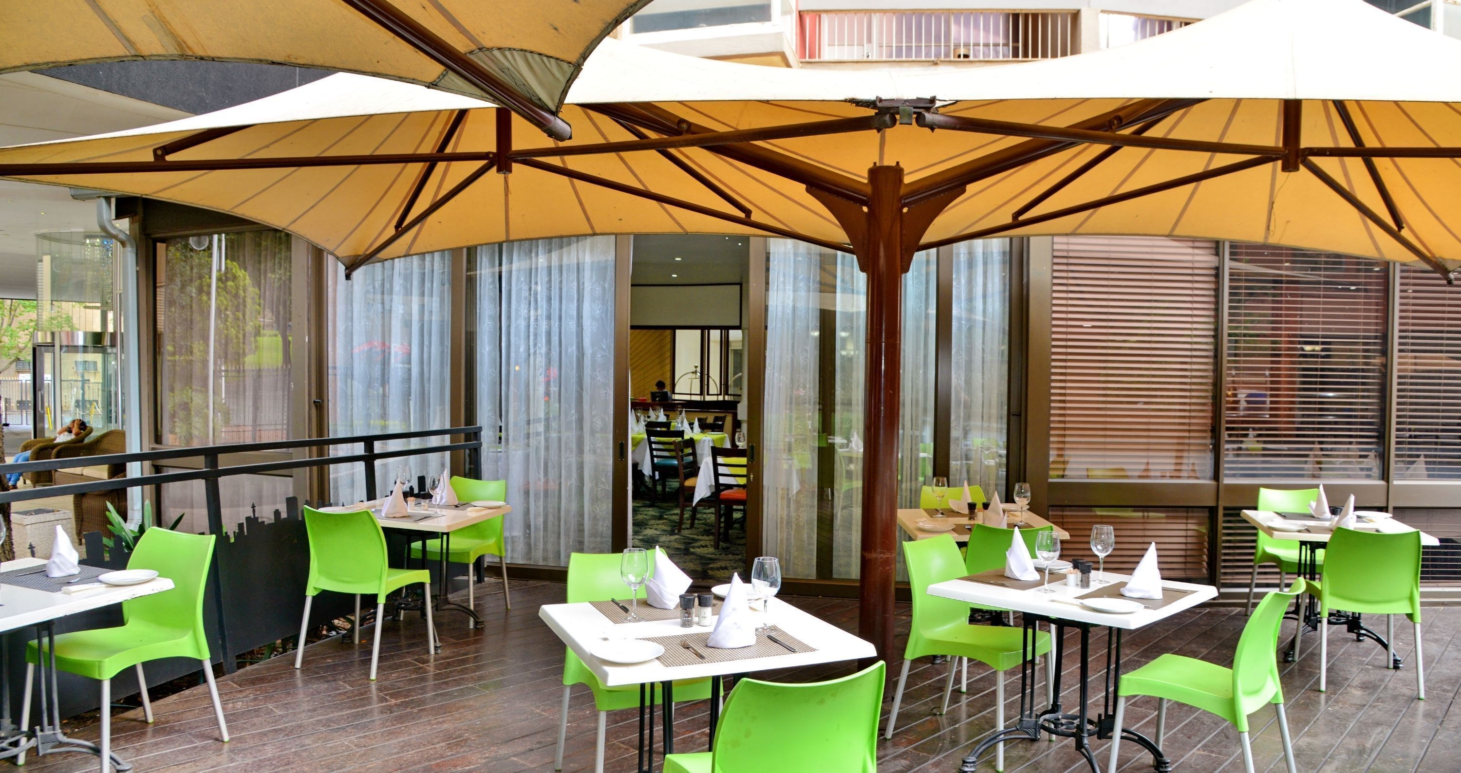 An outdoor dining area with green chairs and tables, covered by large umbrellas.