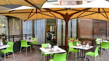 An outdoor dining area with green chairs and tables, covered by large umbrellas.