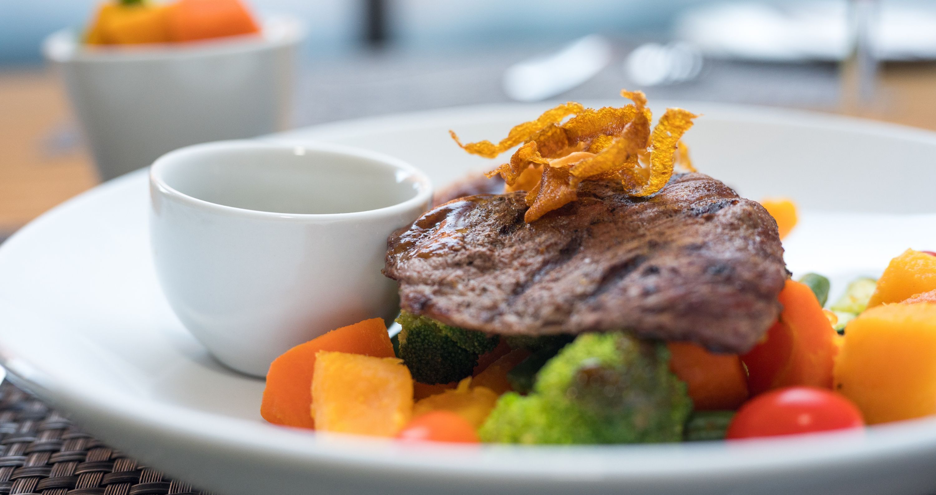 A plate with a steak, vegetables, and a small cup.