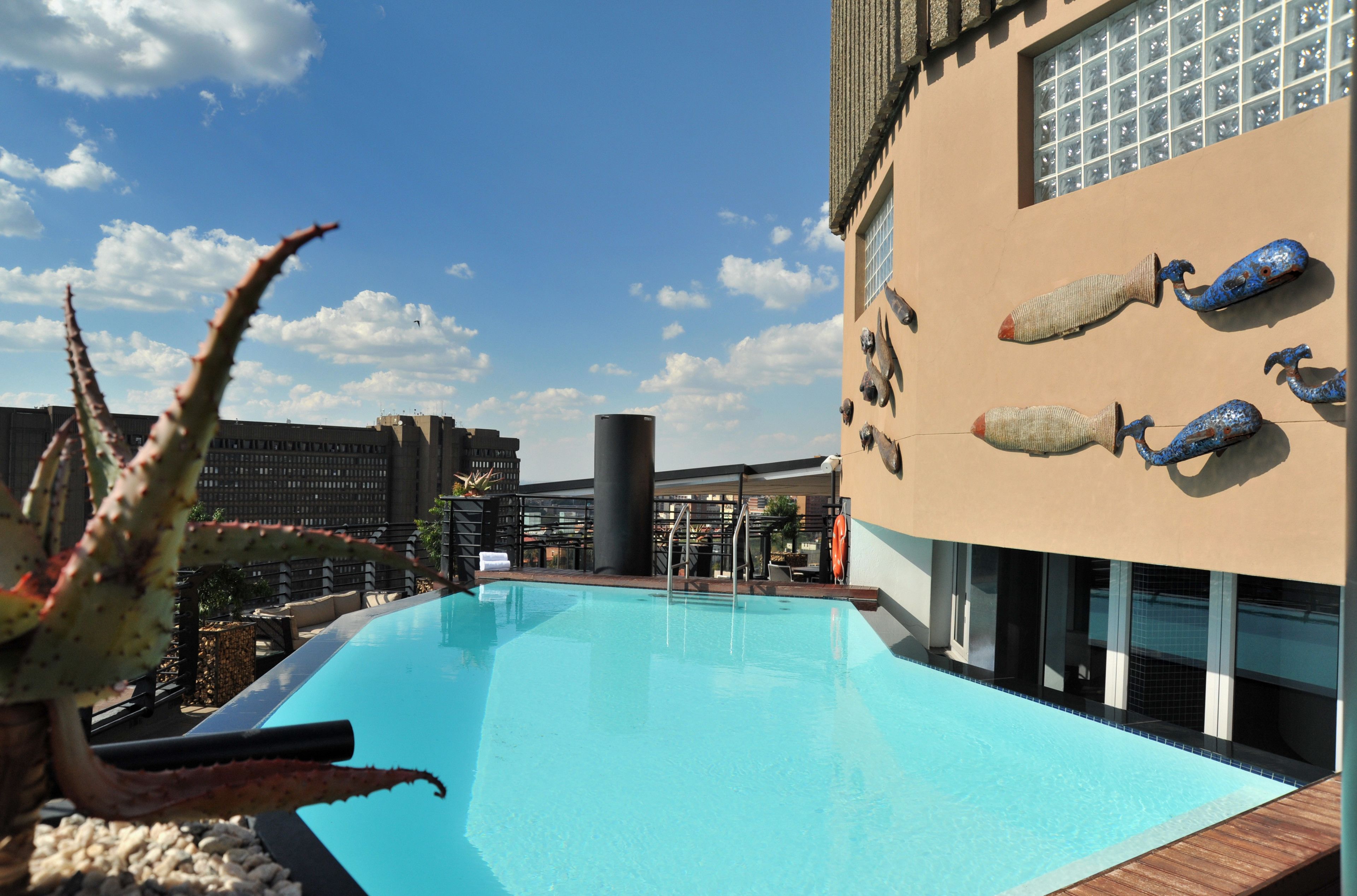 A swimming pool with a clear blue water, surrounded by a modern building with a beige facade and decorative blue and beige vases.
