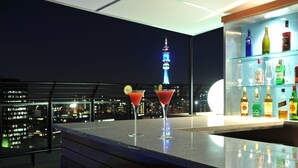 Un bar con dos cócteles rojos, un horizonte urbano y una torre al fondo.
