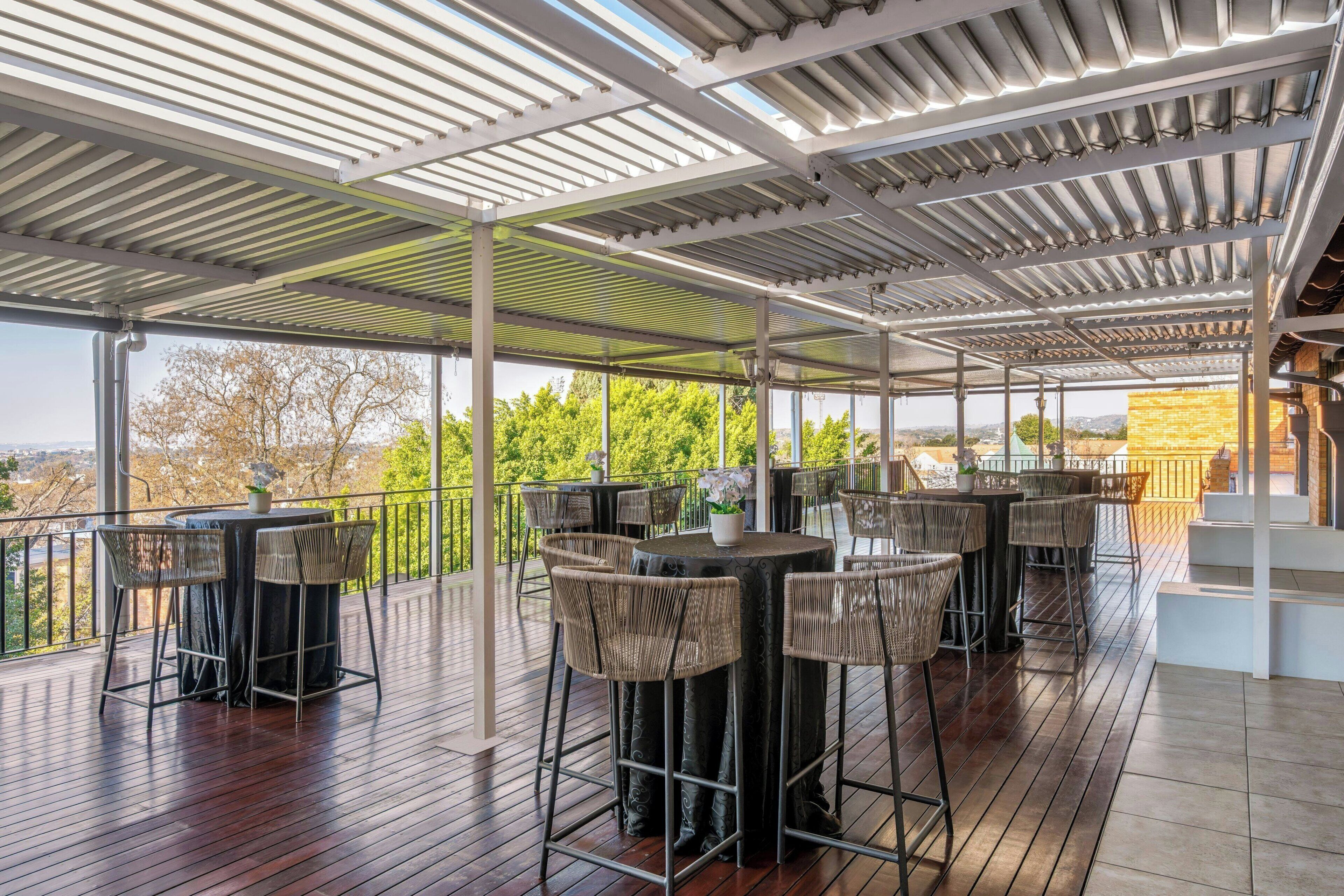 An outdoor covered patio with wooden flooring, wicker furniture, and a view of the landscape.