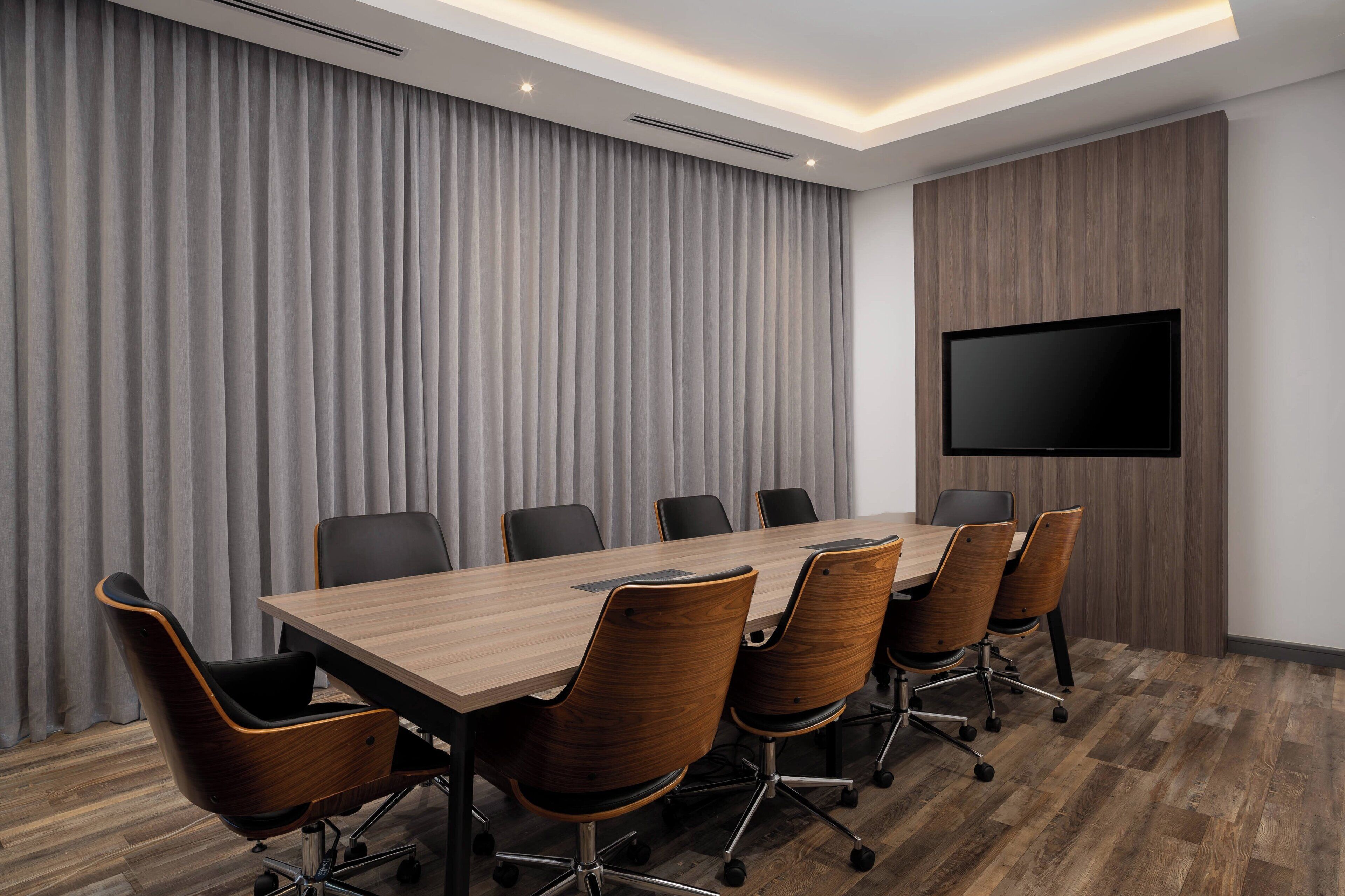 Un salón de conferencias con una mesa larga, seis sillas y un televisor de pantalla plana en la pared.