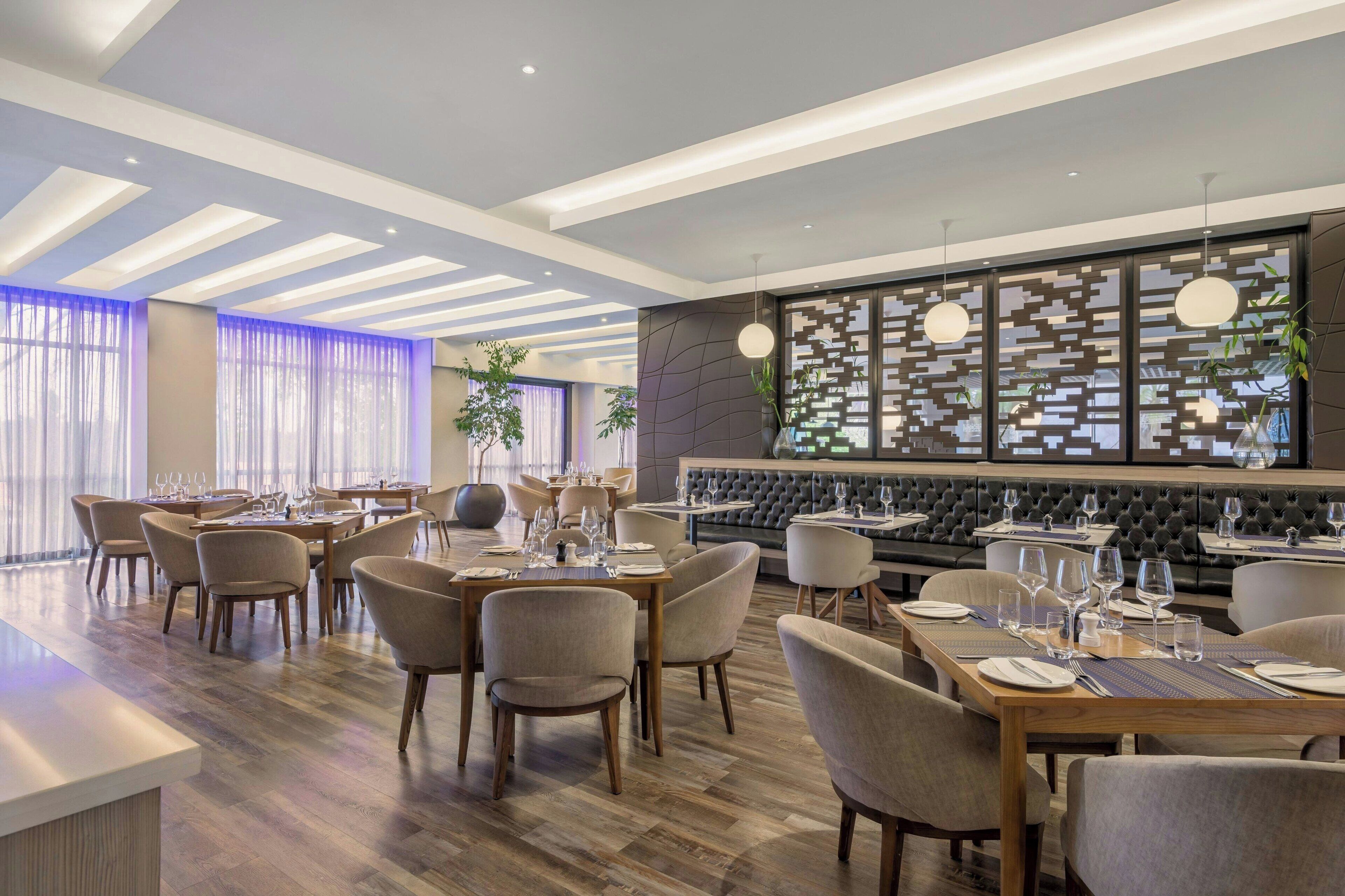 A modern restaurant with wooden tables and chairs, a bar area, and a decorative wall with a geometric pattern.