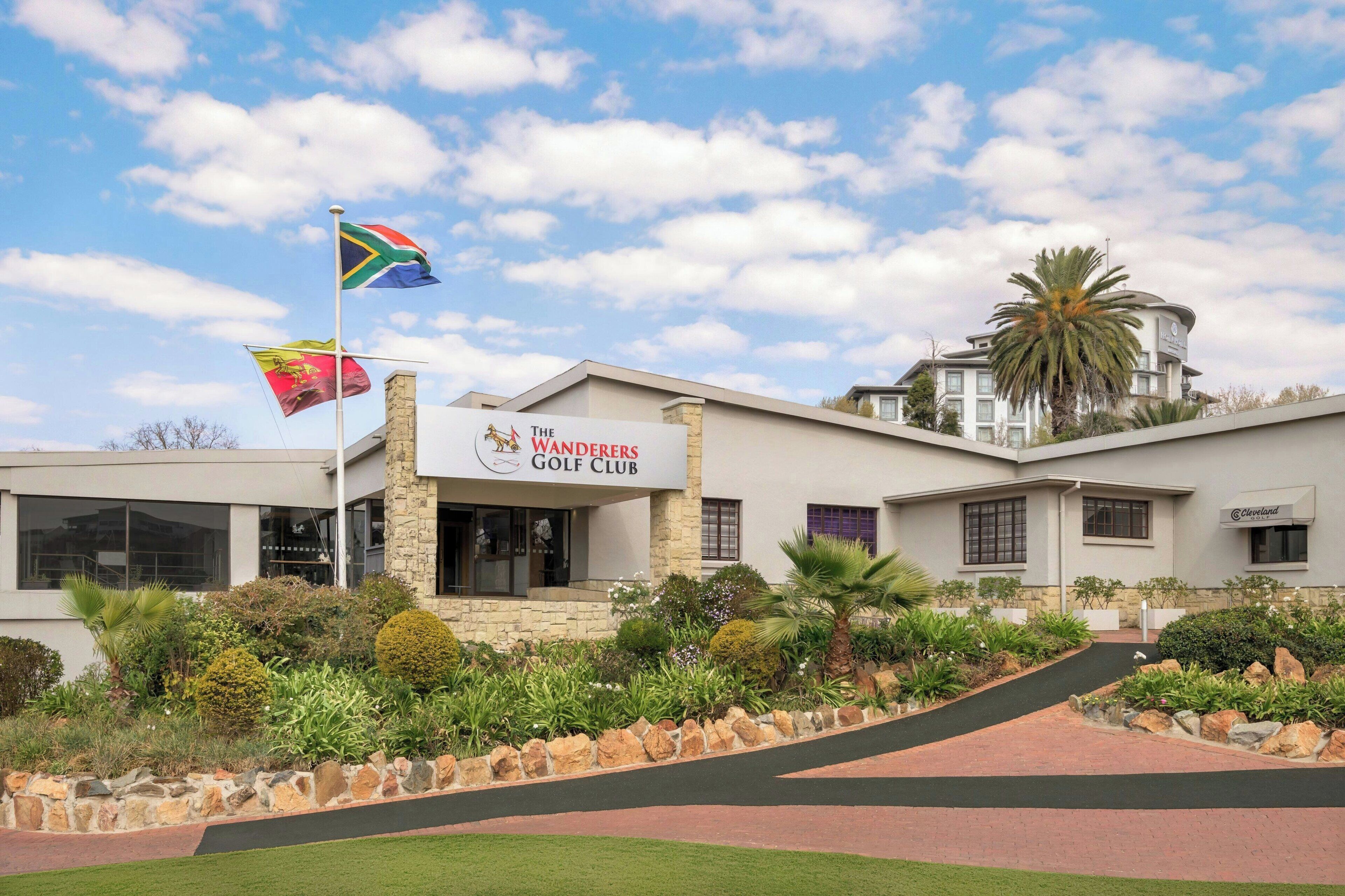 The Wanderers Golf Club with a stone facade, a flagpole with multiple flags, and a well-maintained landscaped area.