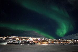 A snow-covered landscape with a town and a mountain in the background. - Funken Lodge (Longyearbyen)