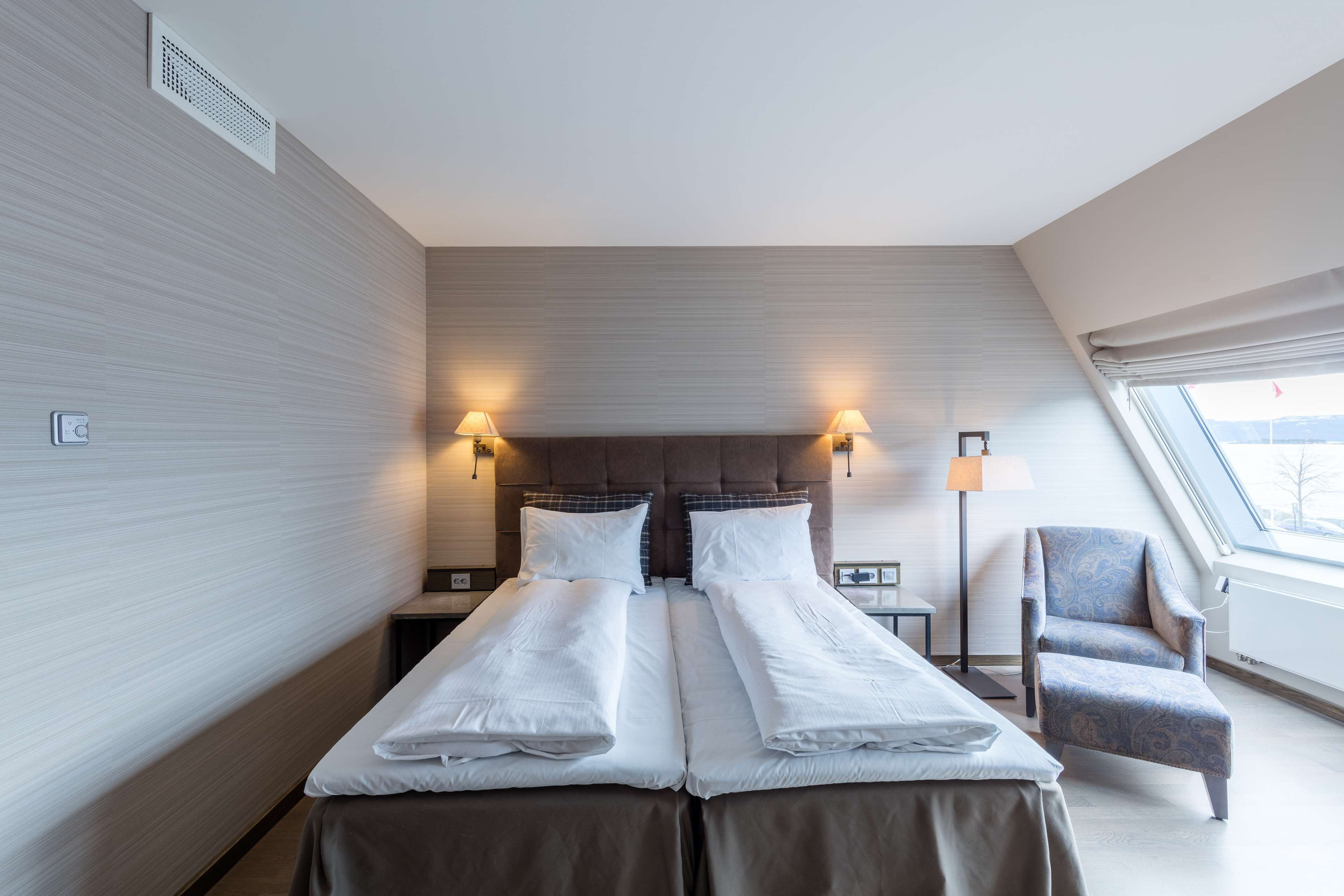 A hotel room with two beds, a chair, and a nightstand with lamps.