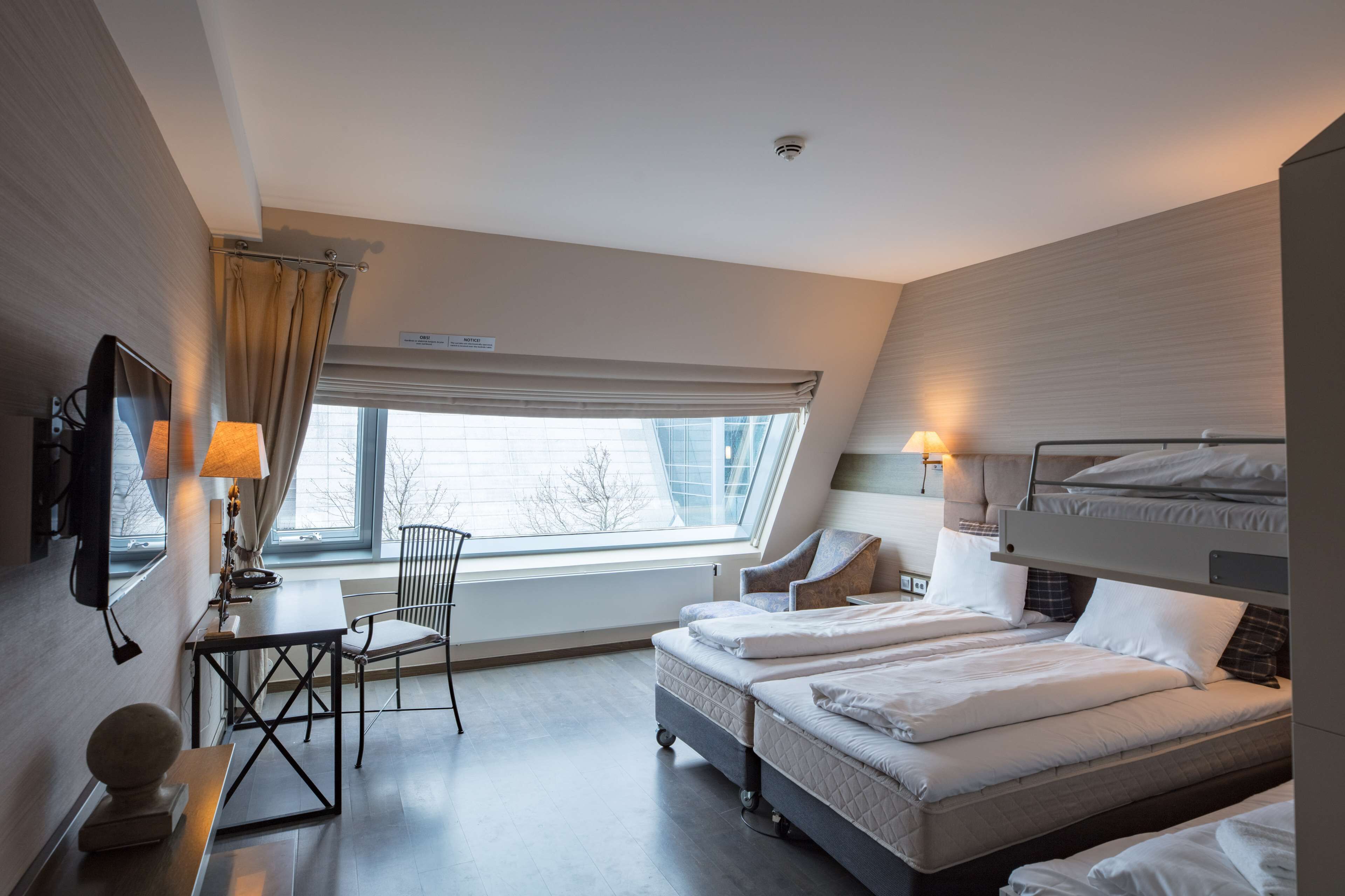 A hotel room with a bed, a desk, a chair, and a window.