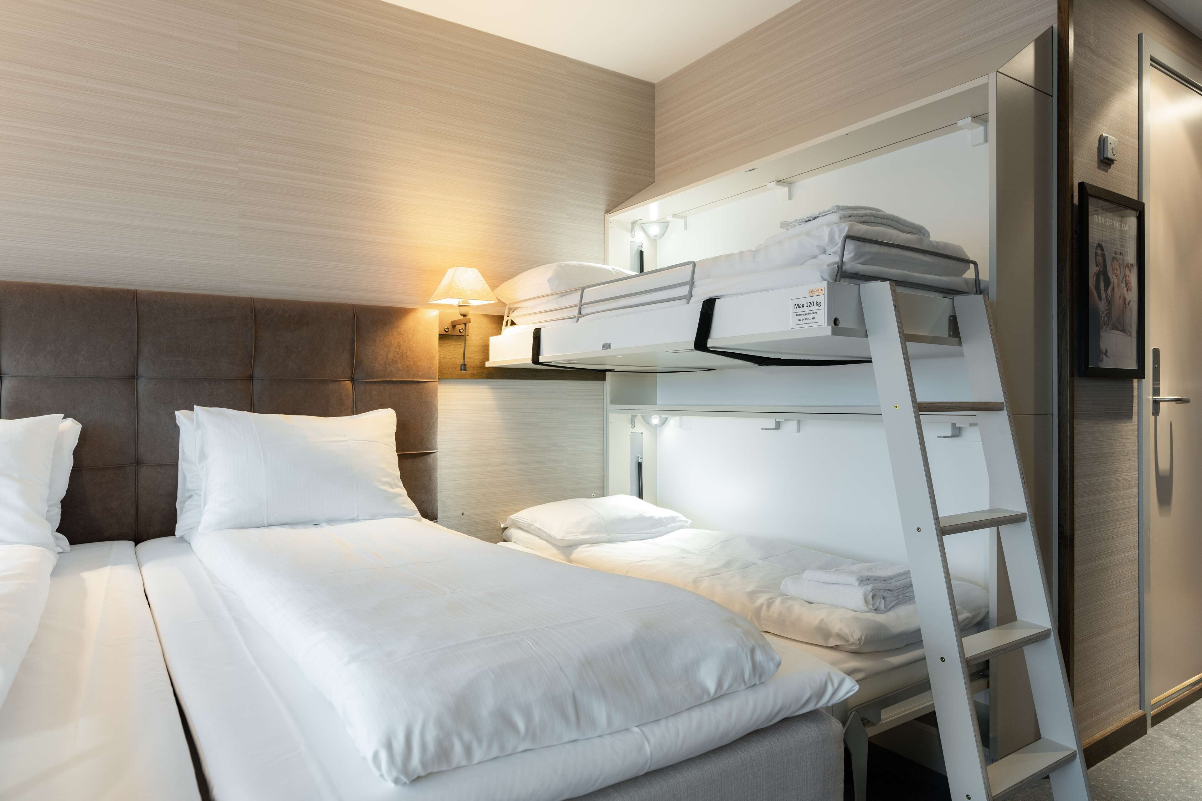 A hotel room with two beds, a ladder, a wall-mounted shelf, and a nightstand with a lamp.
