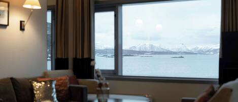 A hotel room with a large window offering a view of snow-capped mountains and a body of water.