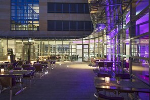 Een eetruimte zowel binnen als buiten met tafels en stoelen, een glazen wand en uitzicht op het interieur van het gebouw.