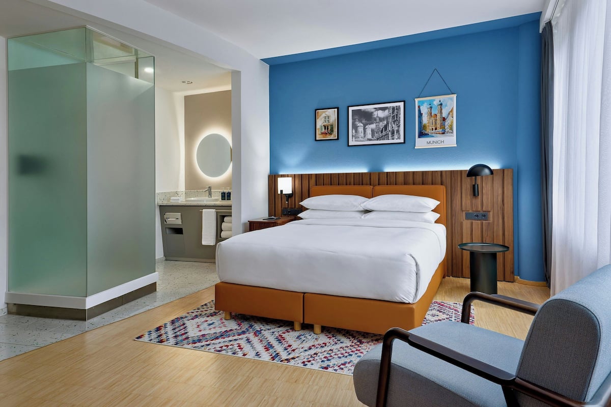 A hotel room with a bed, a desk, and a chair. There are two framed pictures on the wall.