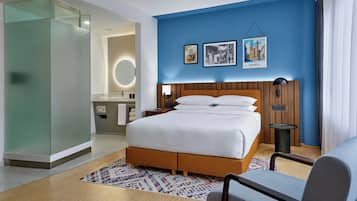 A hotel room with a bed, a desk, and a chair. There are two framed pictures on the wall.