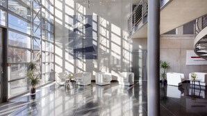 En rymlig entréhall med ett välpolerat golv, moderna sittmöbler och stora fönster som släpper in naturligt ljus.