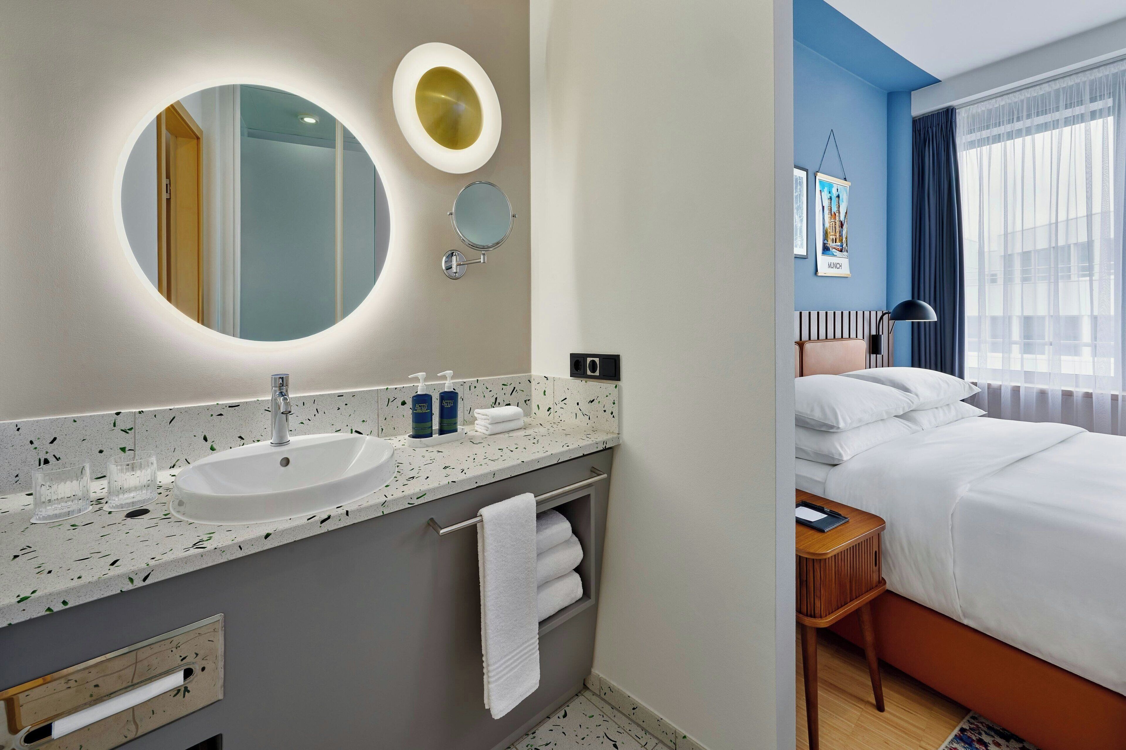 A modern hotel bathroom with a round mirror, a sink, and a towel rack.