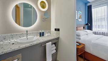 A modern hotel bathroom with a round mirror, a sink, and a towel rack.