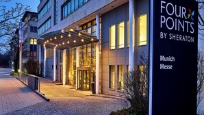 En hotellentrén med en överbyggd gång, glasdörrar och en skylt som visar ”FOUR POINTS BY SHERATON Munich Messe”.