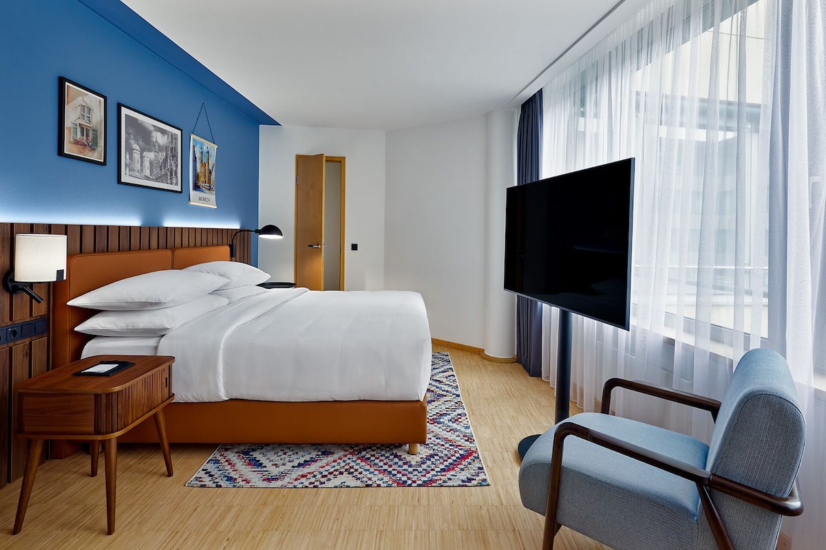 A hotel room with a bed, a desk, a chair, a TV, and a window with curtains.