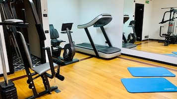 Un gimnasio con equipo de ejercicio, una cinta de correr y colchonetas azules en el suelo.