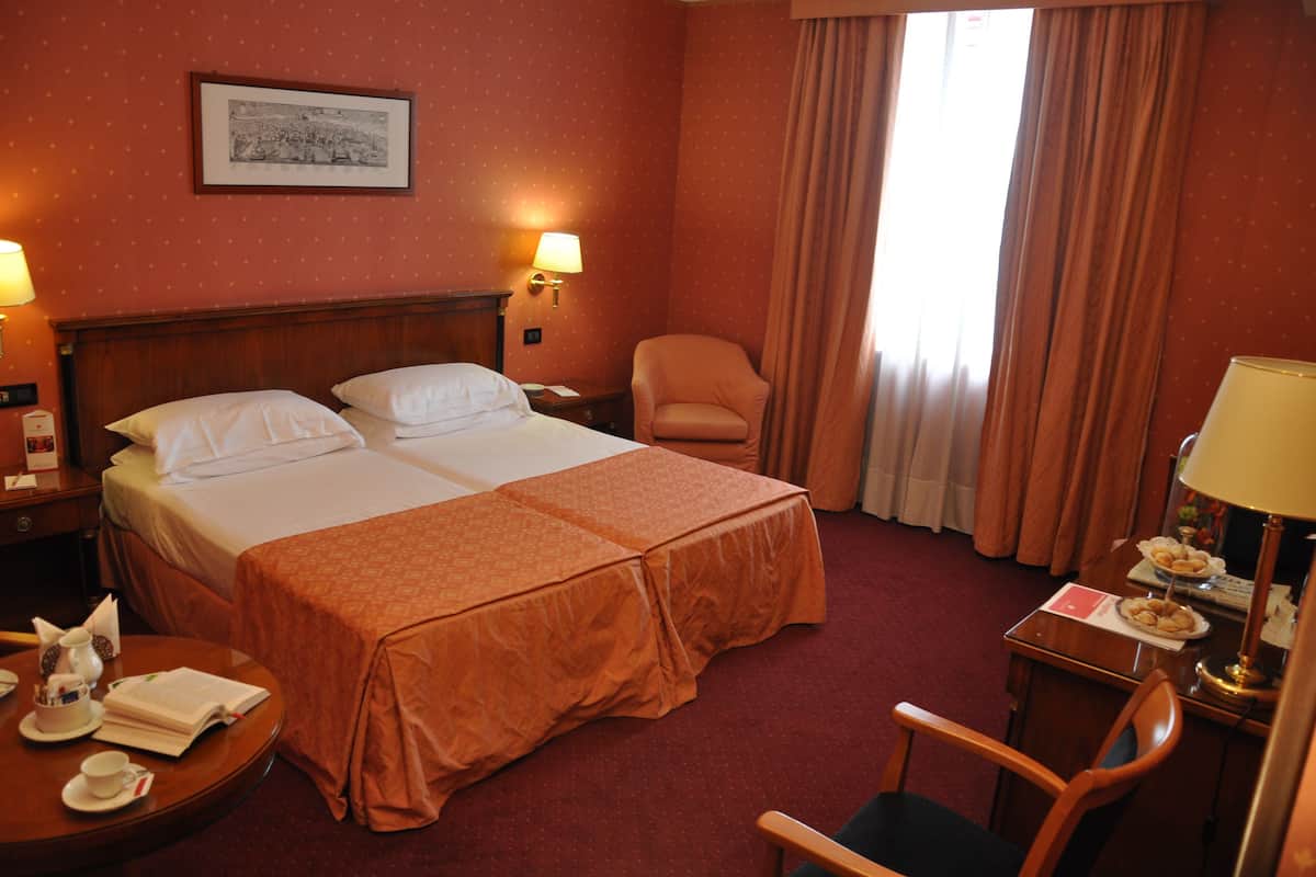 Une chambre d’hôtel avec deux lits, une chaise, une table avec une lampe et un tableau au mur.