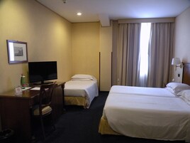 Een hotelkamer met twee enkele bedden, een bureau met stoel, een televisie en een raam met gordijnen.