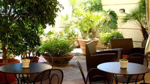 An outdoor patio with round tables and chairs, surrounded by various potted plants and a large tree. - Ramada by Wyndham Naples (Naples)