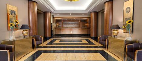 A hotel lobby with a reception desk, check-in counters, and a patterned floor.