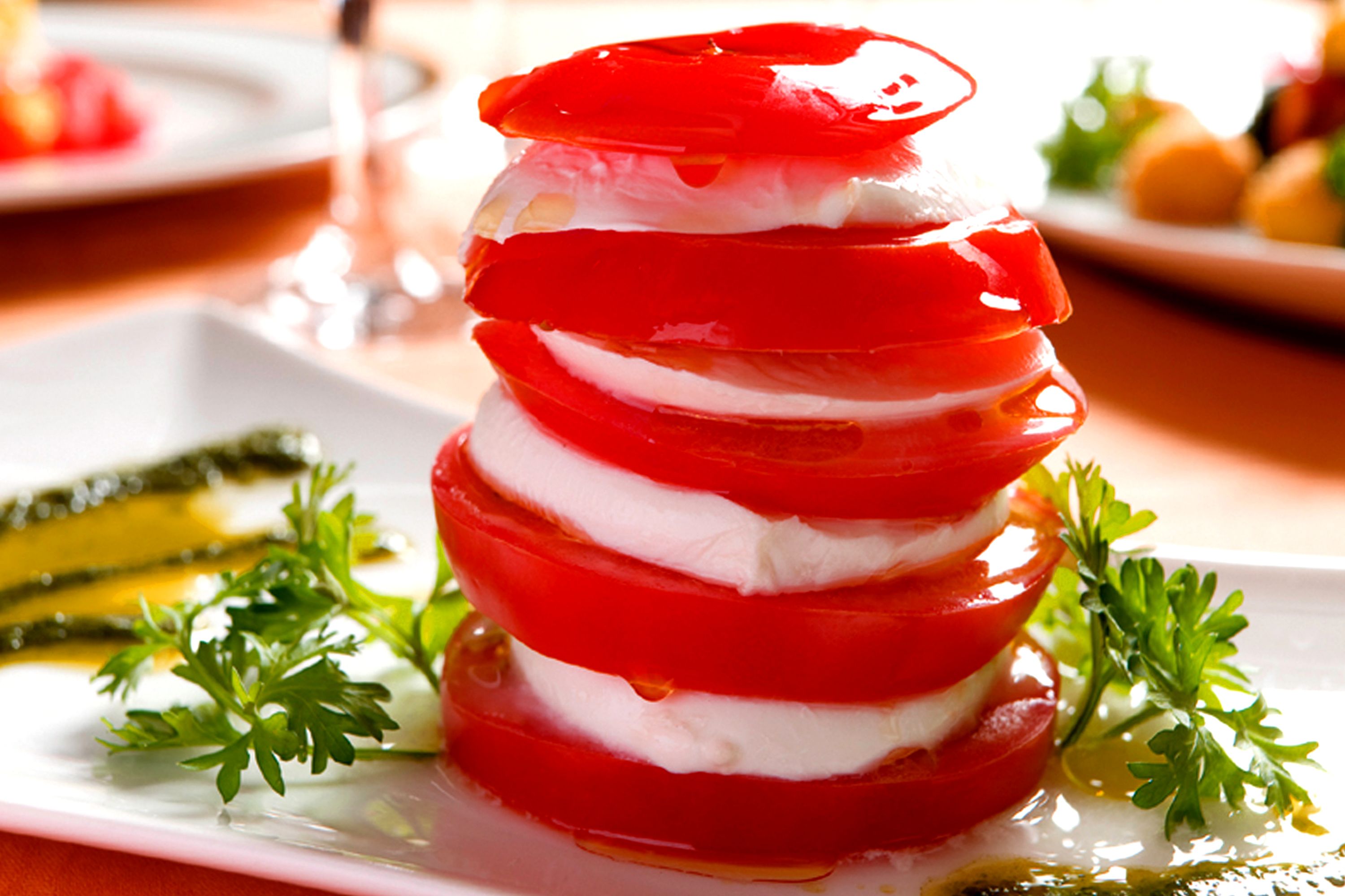 Un plato blanco con un guiso en capas de tomates y queso, adornado con perejil.