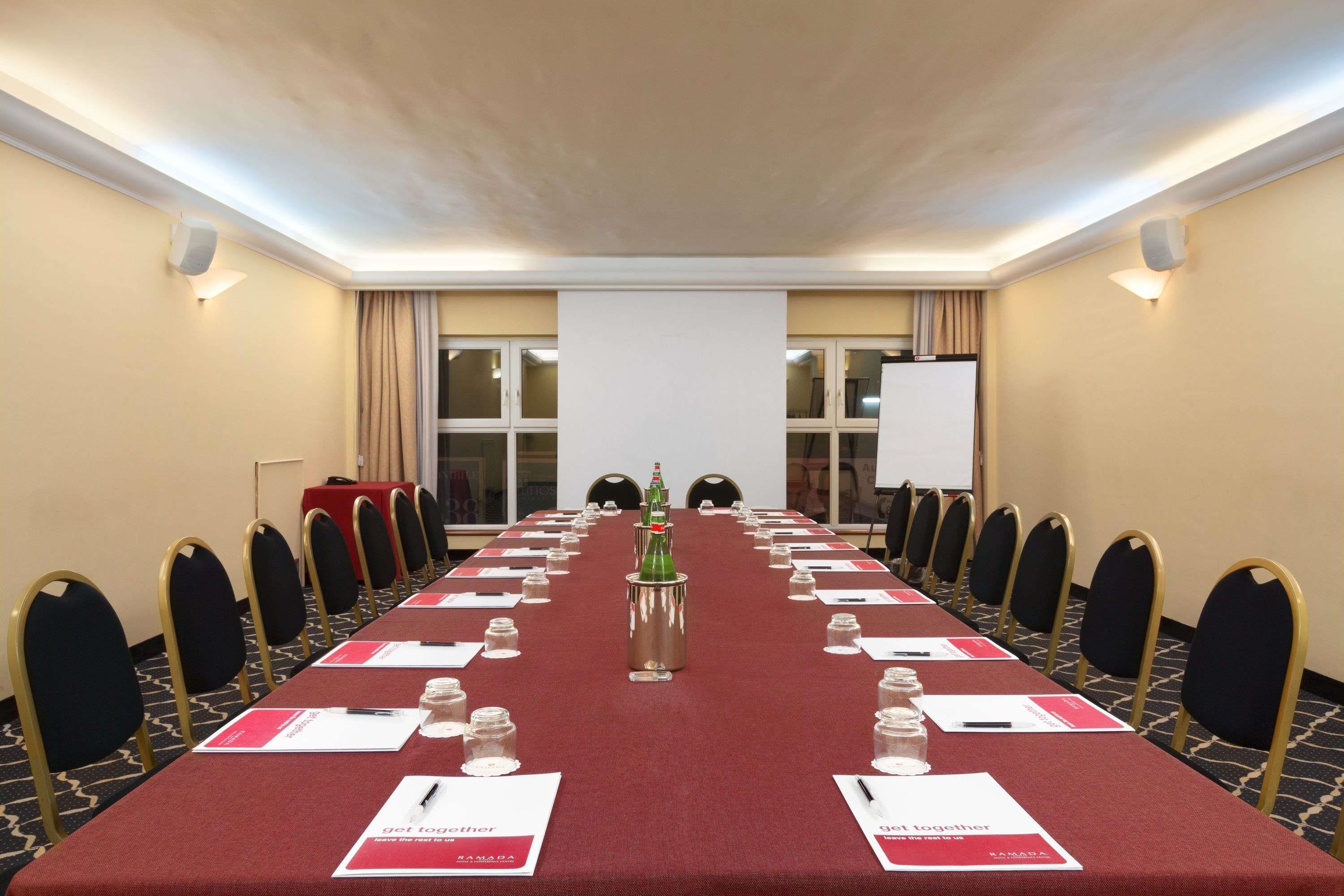 Ein Konferenzraum mit einem langen Tisch, Stühlen, Namensschildern und einer Projektionsleinwand.