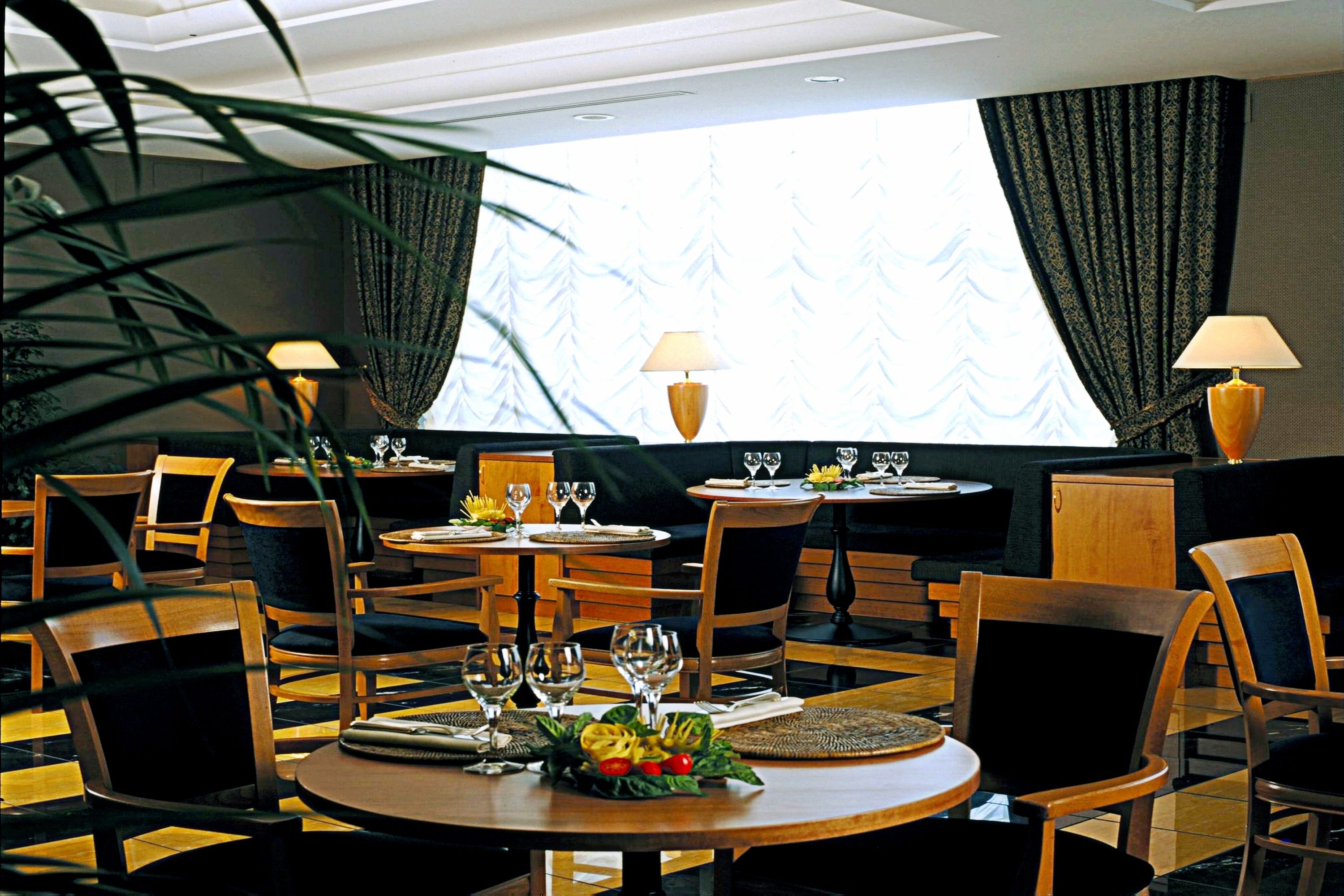 A restaurant with round tables, chairs, and a large window with curtains.