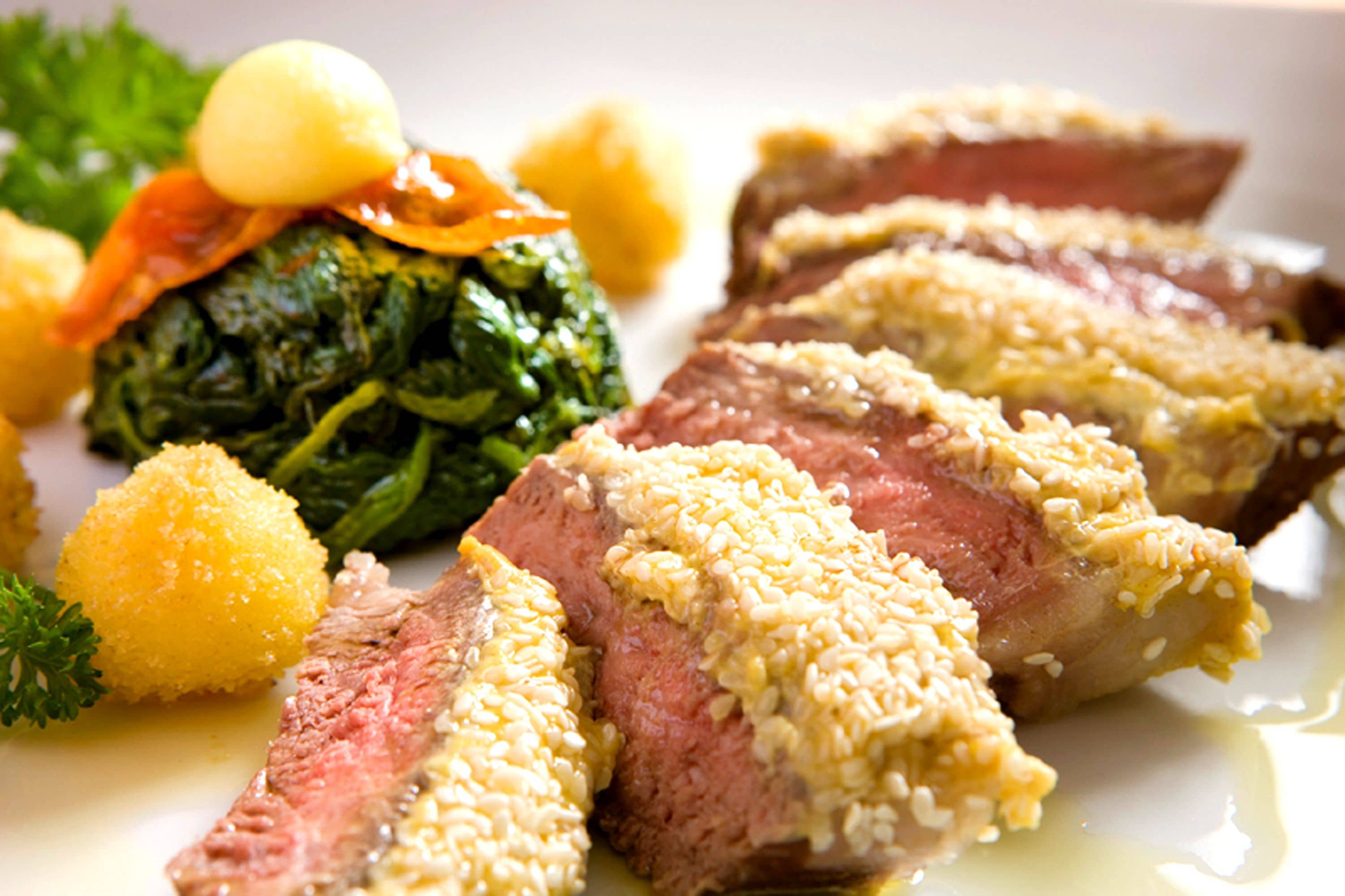 A plate of food with sliced meat, greens, and potatoes.