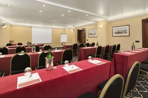 Una sala conferenze con diversi tavoli, sedie, cartellini dei partecipanti e uno schermo per proiettore.
