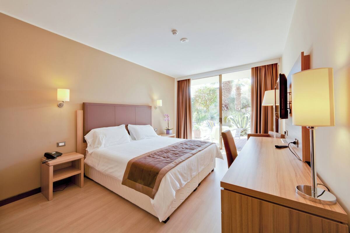 Ein Hotelzimmer mit Bett, Nachttisch, Lampe und Schreibtisch mit Stuhl.